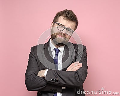 Friendly Caucasian bearded man in glasses and a suit stands with crossed arms and smiles cutely. Pink background. Stock Photo