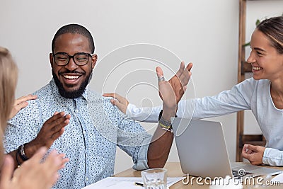 Friendly caucasian team employees tap african colleague on shoulder Stock Photo