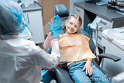 Friendly dentist giving high five little girl sitting on stomatological chair after treatment Stock Photo