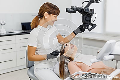 Friendly dentist talking to patient during teeth examination with microscope. Modern dental clinic. Concept of Stock Photo