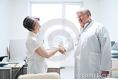 Friendly doctor greets with handshake elderly woman in medical office Stock Photo
