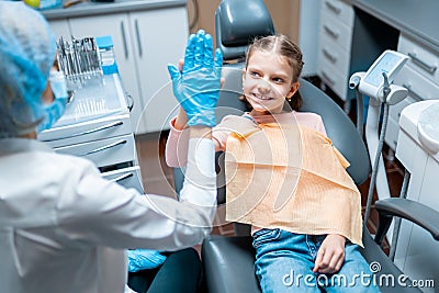 Friendly female dentist giving high five little girl sitting on stomatological chair after treatment Stock Photo