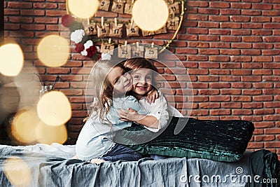 Friendly hugs. Little girls having fun on the bed with holiday interior at the background Stock Photo