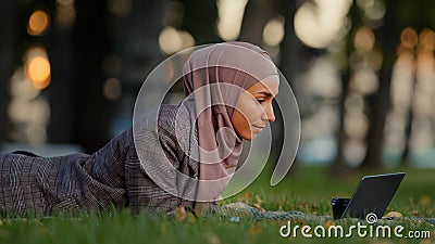 Friendly islamic business woman muslim girl in hijab lying grass lawn in park outdoors female teacher online mentor Stock Photo