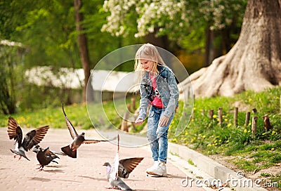 Friendly joyful girl child feeds pigeons in city summer park Stock Photo