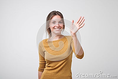 Friendly-looking european teenager dressed in yellow pulover saying hello, waving her hand. Stock Photo