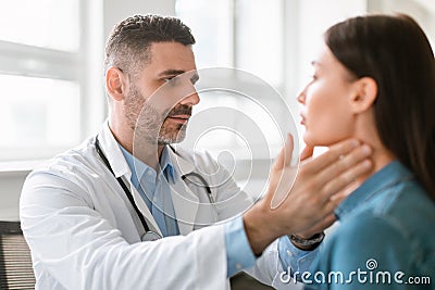 Friendly middle aged male doctor checking sore throat or thyroid glands, touching neck of young female patient Stock Photo