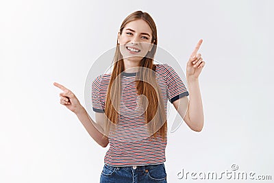 Friendly, pleasant cheerful woman in striped t-shirt with long fair hair, raise hands pointing sideways, show left and Stock Photo