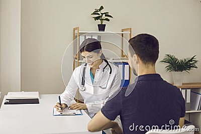 Friendly practitioner smiling and writing down prescription for young male patient Stock Photo