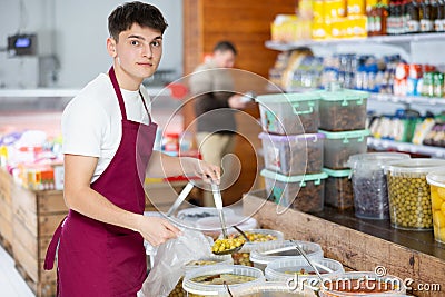 Friendly salesman in an apron offers to buy pickled green olives in grocery supermarket Stock Photo