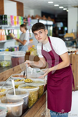 Friendly salesman in an apron offers to buy pickled green olives in grocery supermarket Stock Photo