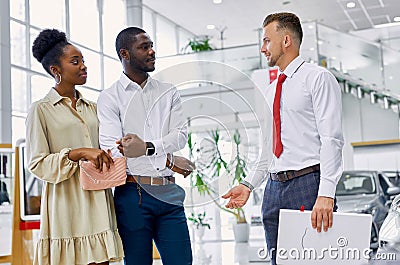 Friendly salesman and beautiful couple in car showroom Stock Photo