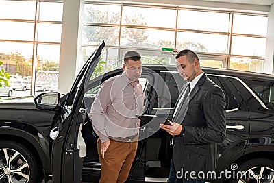 friendly salesman with male client talking and explaining new car before sale or rent in dealership Stock Photo