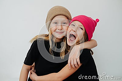 Friendly siblings in colorful hats hugging, touching their cheeks. Stock Photo