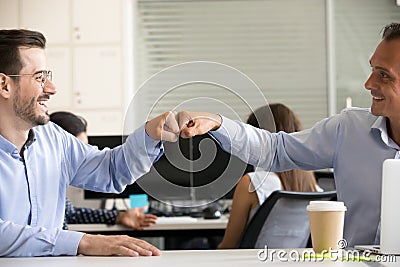 Friendly smiling male colleagues fist bumping at workplace close up Stock Photo