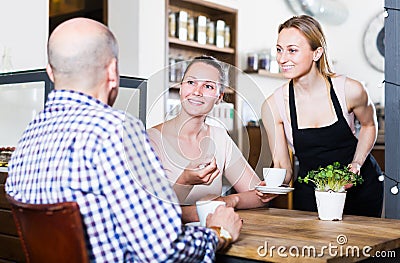 friendly waiter girl brought cup of coffee for couple of different aged people Stock Photo