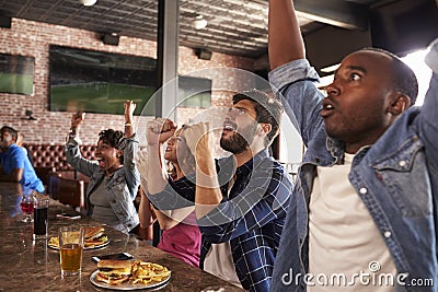 Friends At Counter In Sports Bar Watch Game And Celebrate Stock Photo