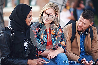 Friends, diversity and happy people with communication and connection outdoor on stairs. Hijab, muslim and talking women Stock Photo