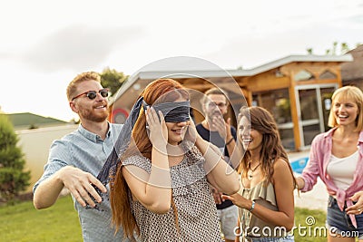 Friends having fun playing blind man`s buff while at poolside summertime outdoor party Stock Photo