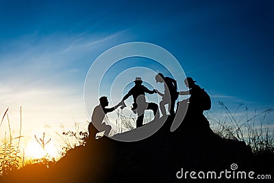 friends helping each other and with teamwork trying to reach the top of the mountains during wonderful summer sunset Stock Photo