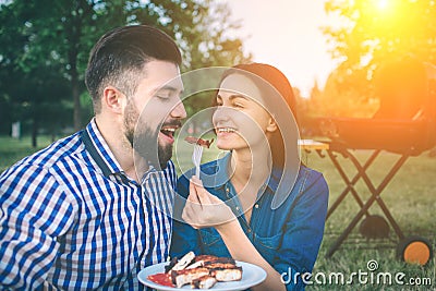 Friends making barbecue and having lunch in the nature. Couple having fun while eating and drinking at a pic-nic - Happy Stock Photo