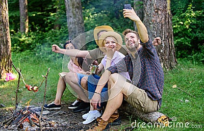 Friends near bonfire enjoy vacation and roasted food. Tourists sit log near bonfire taking selfie photo smartphone Stock Photo