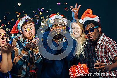 Friends at New Year`s party, wearing santa hats, dancing and blowing confetti Stock Photo