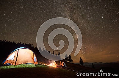 Friends resting beside camp, campfire under night starry sky Stock Photo