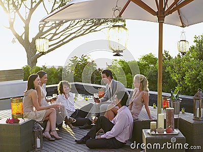 Friends sitting on porch Drinking and socialising under umbrella Stock Photo