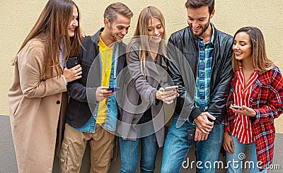 Friends standing by a wall background and using their smarphones - Young people on social media Stock Photo