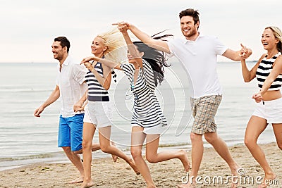 Friends in striped clothes running along beach Stock Photo