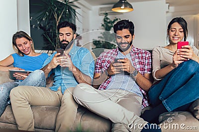 Friends using electronic devices while sitting on sofa Stock Photo