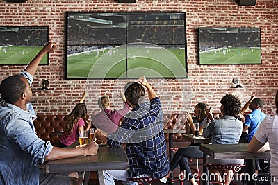 Friends Watching Game In Sports Bar On Screens Celebrating Stock Photo