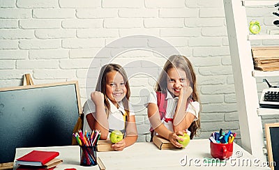 Friendship of small sisters in classroom at knowledge day. Happy school kids at lesson in september 1. Little girls eat Stock Photo