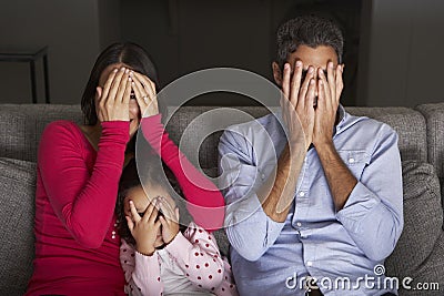 Frightened Hispanic Family Sitting On Sofa And Watching TV Stock Photo