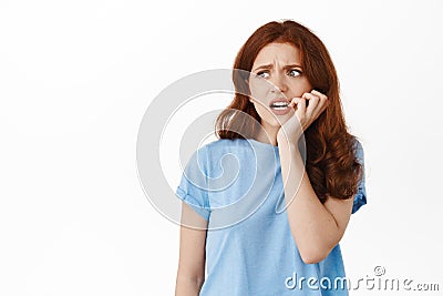 Frightened redhead woman biting fingernails and looking left with anxious face, fear of something, standing worried and Stock Photo