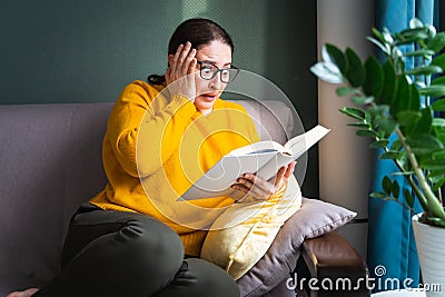 Shocked scared woman reading scary horror novel or thriller book at home Stock Photo