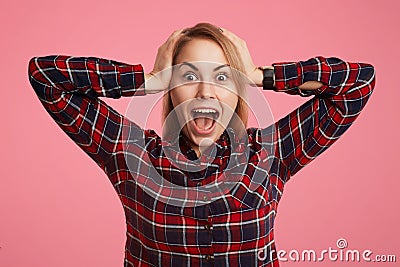 Frightened shocked young female opens mouth widely and exclaims in terror, doesn`t anticipate to see her phobia, keeps hands on he Stock Photo