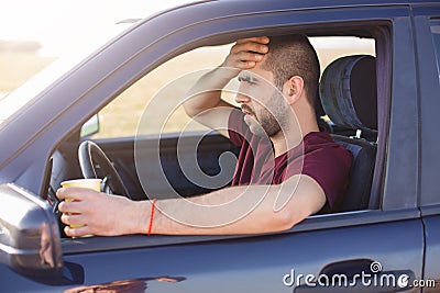 Frightened terrified dark haired unshaved man, stops his car on side of road, drinks tea, sees with shock through windshield at Stock Photo