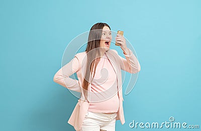 frightened pregnant woman on blue background calls by mobile phone, discharge of amniotic fluid, the beginning of labor Stock Photo