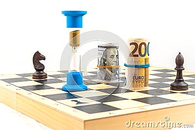 Front angle view of chess board with two black chess pieces, an hourglass with falling sand within and rolled euro bank Stock Photo