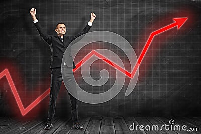 Front full length view of happy businessman raising arms in triumphant gesture with red graph arrow going up behind him Stock Photo
