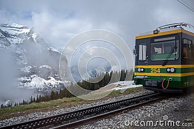 The front of green with yellow hiking train, Jungfrau, with beautiful view of foggy mountain background Editorial Stock Photo