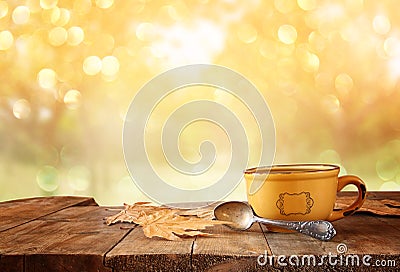 Front image of coffee cup over wooden table and autumn leaves in front of autumnal sunset background Stock Photo