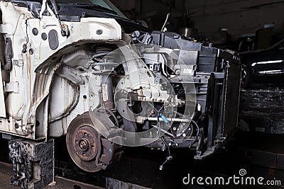 The front part of the car after an accident in a car repair service with a disassembled hood and metal grille and various parts in Stock Photo