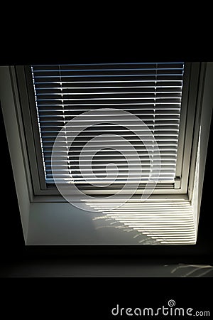 A front portrait of a velux roof window with a half open jalousie in it to keep the sun and warmth out or to keep the light from Stock Photo