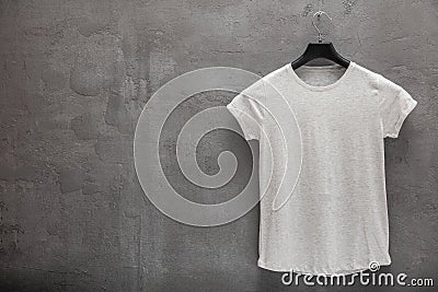 Front side of female grey melange cotton t-shirt on a hanger and a concrete wall in the background Stock Photo