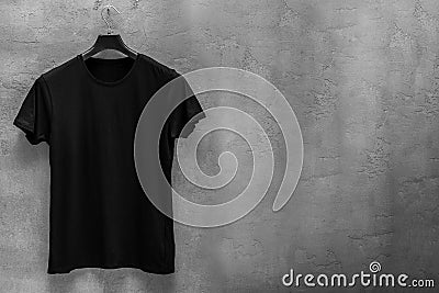 Front side of male black cotton t-shirt on a hanger and a concrete wall in the background Stock Photo