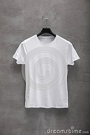 Front side of male white cotton t-shirt on a hanger and a concrete wall in the background Stock Photo