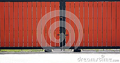 Front veiw of a red wooden slats Sliding gate with a black metal handle in the from of a fence Stock Photo